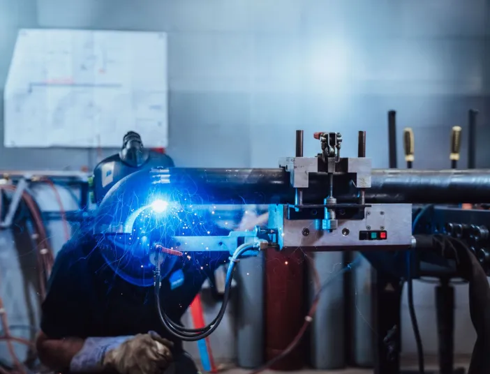Ein Mechatroniker führt eine präzise Schweißarbeit an einem großen Metallrohr mit Hilfe einer automatisierten Vorrichtung durch.