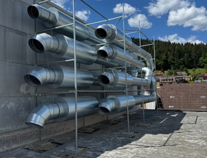 Mehrere große Lüftungsrohre aus glänzendem Metall sind ordentlich in einem Gerüst an der Außenwand eines Industriegebäudes montiert.