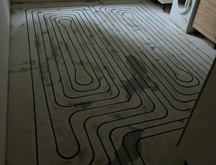 Ein Raum mit teilweise eingebauter Küche zeigt den frisch vorbereiteten Boden für eine Fußbodenheizung, bei der die Heizungsrohre bereits in das Estrichbett eingelassen sind.