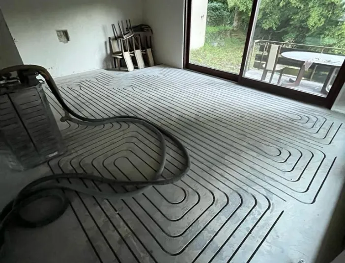 Das Bild zeigt einen Raum im Rohbauzustand mit bereits verlegten Heizungsrohren für eine Fußbodenheizung im Estrich.