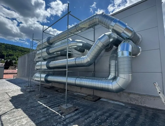 Ein modernes Lüftungssystem mit glänzenden Metallrohren verläuft in mehreren Ebenen entlang der Fassade eines Industriegebäudes.