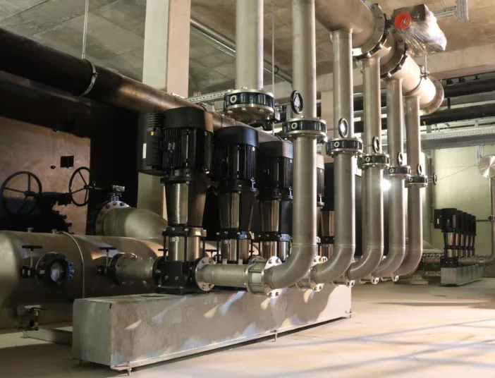 Das Bild zeigt eine moderne Pumpenanlage mit mehreren vertikal montierten Edelstahlpumpen der Grundfos-CR-Serie.