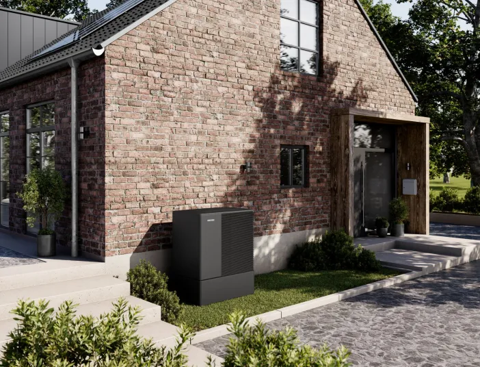 Die Premiumwaermepumpe Stibel-Eltron WPL A steht auf einer kleinen Rasenfläsche vor einem restausrierten Backsteinhaus.