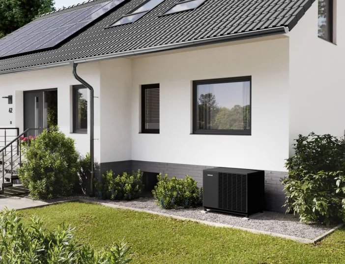 Eine schwarze Waermepumpenaußeneinheit von Stiebel-Eltron steht auf einem Kiesbett vor einem Einfamilienhaus.