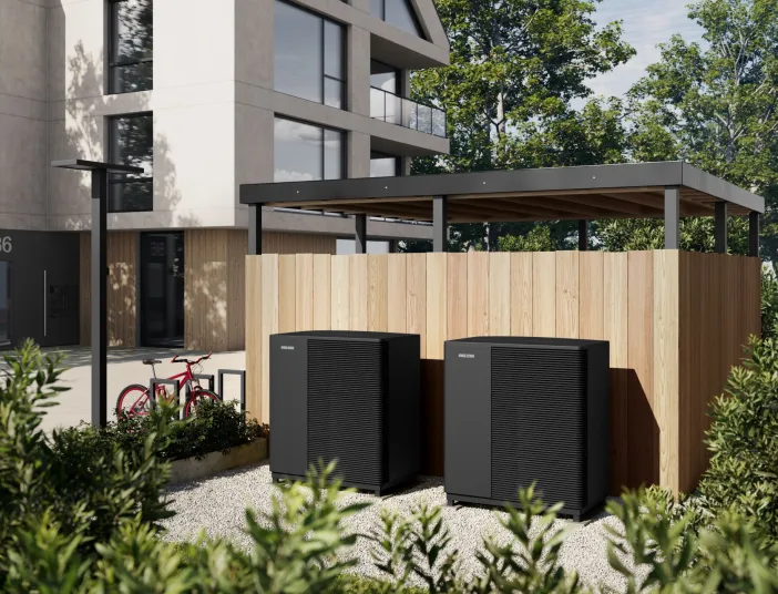 Zwei Waermepumpen-Außenheiten von Stiebel-Eltron stehen neben einem Mehrfamilienhaus vor einer Holzwand.