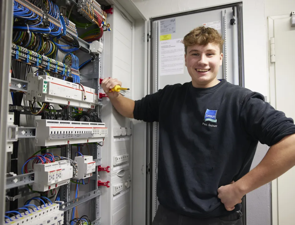 Auszubildender Elektriker arbeitet an einem geöffneten Schaltschrank mit Verkabelung und Steuerungstechnik.