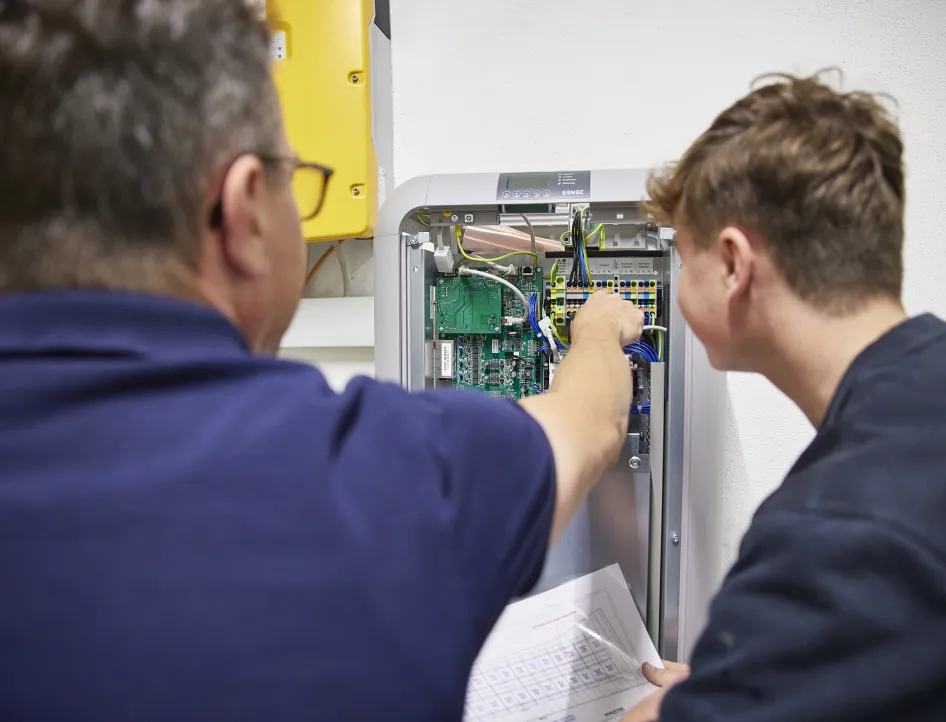 Elektriker erklärt einem Auszubildenden die Verkabelung und Steuerung in einem geöffneten Schaltschrank.