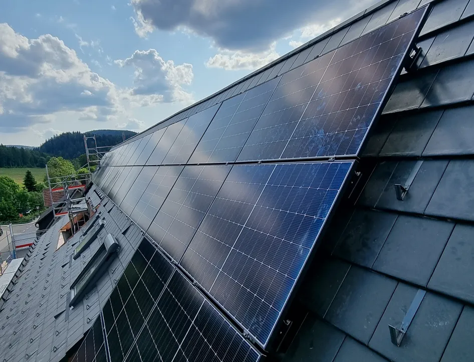 Installierte Photovoltaikmodule auf einem Hausdach während der Montage unter blauem Himmel.